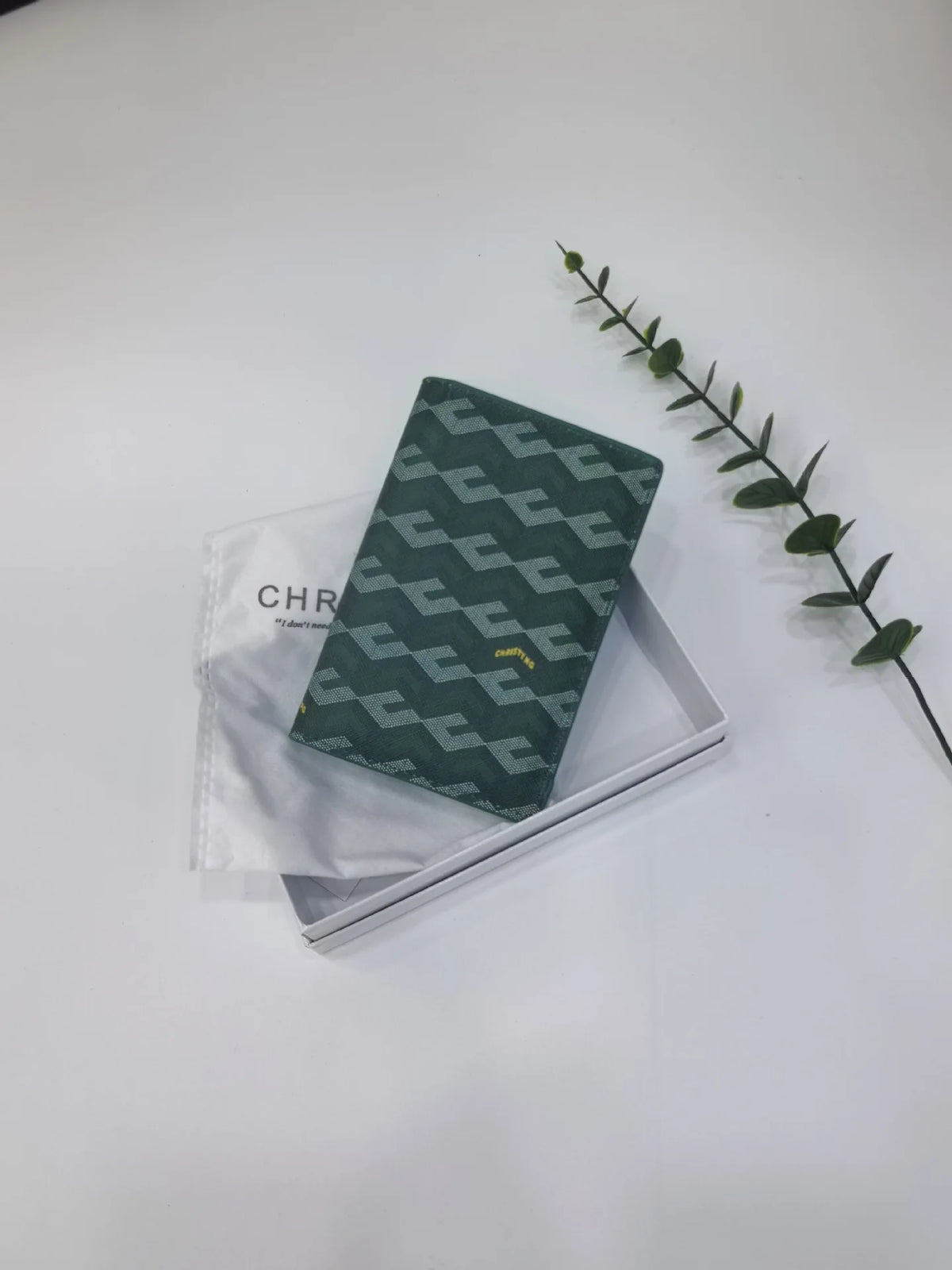 A dark green geometric print passport wallet resting on a white surface next to a leafy green branch.