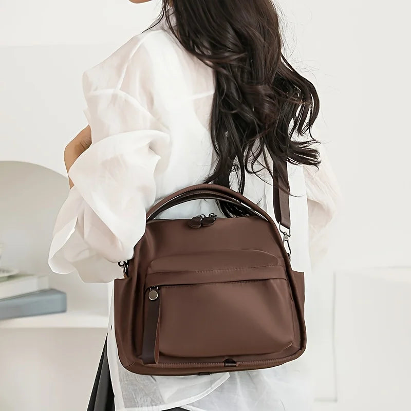 A woman is holding a brown multi-pocket shoulder crossbody bag with white sheer fabric over her white top.