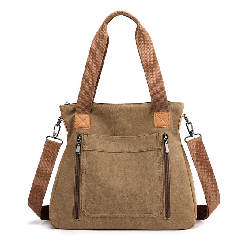 A tan canvas tote bag with brown leather handles and pockets shown against a white background.