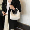 A person wearing a black shirt and light pants holds a cream woven embossed hobo shoulder bag with a top handle.