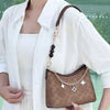A model wears a white shirt over a white top and holds a brown leather crossbody bag with a gold chain detail.