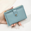 A hand holds a light blue card holder wallet with a gold zipper and silver-toned snap closure.