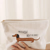 A cream-colored makeup storage bag with a corduroy sausage dog pattern is held by a hand.
