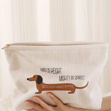 A cream-colored makeup storage bag with a corduroy sausage dog pattern is held by a hand.