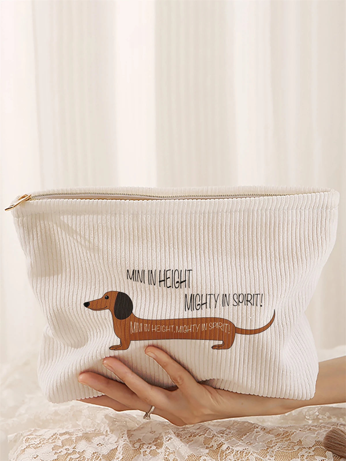 A cream-colored makeup storage bag with a corduroy sausage dog pattern is held by a hand.