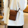 A close-up of a brown vintage PU leather crossbody bag worn by a person in a white blazer.