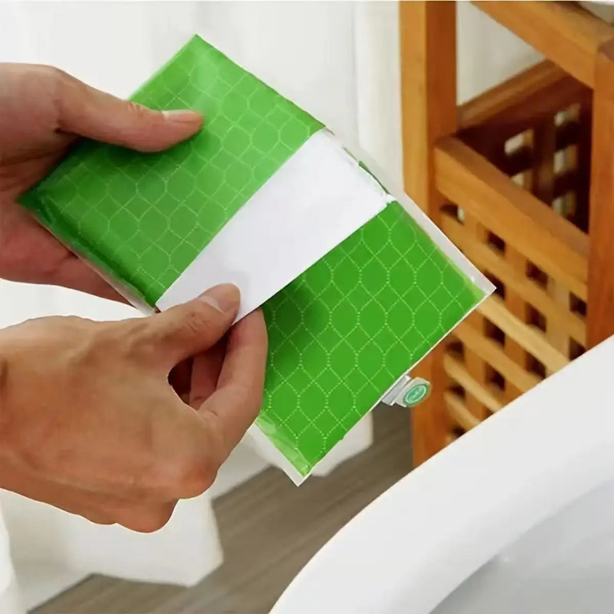 Hands are placing a green disposable toilet seat cover onto a white toilet seat.