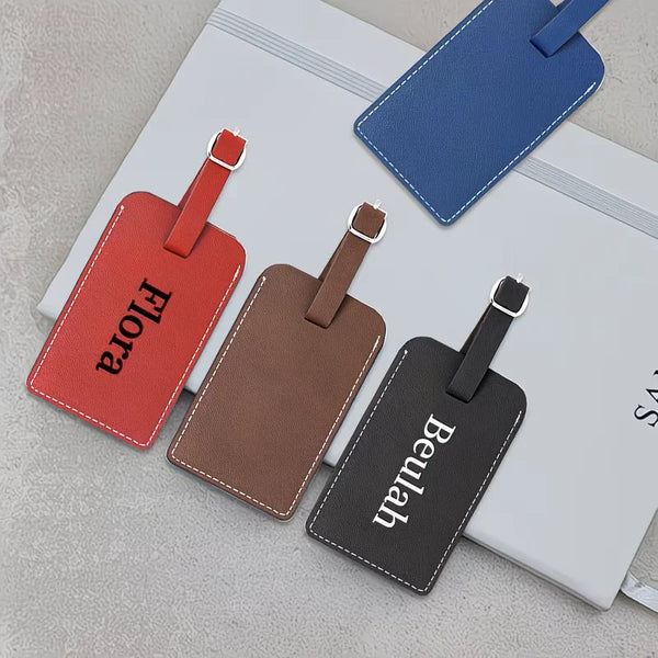 A set of three faux leather passport and luggage tags in red, brown, and black with leather straps