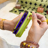 A hand holds a lime green and purple cartoon character coin purse wallet against a patterned fabric background.