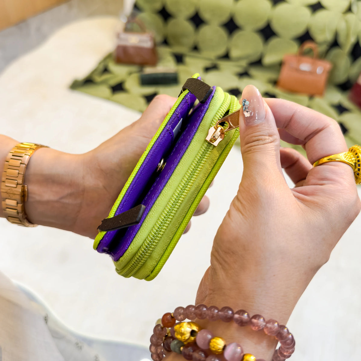 A hand holds a lime green and purple cartoon character coin purse wallet against a patterned fabric background.