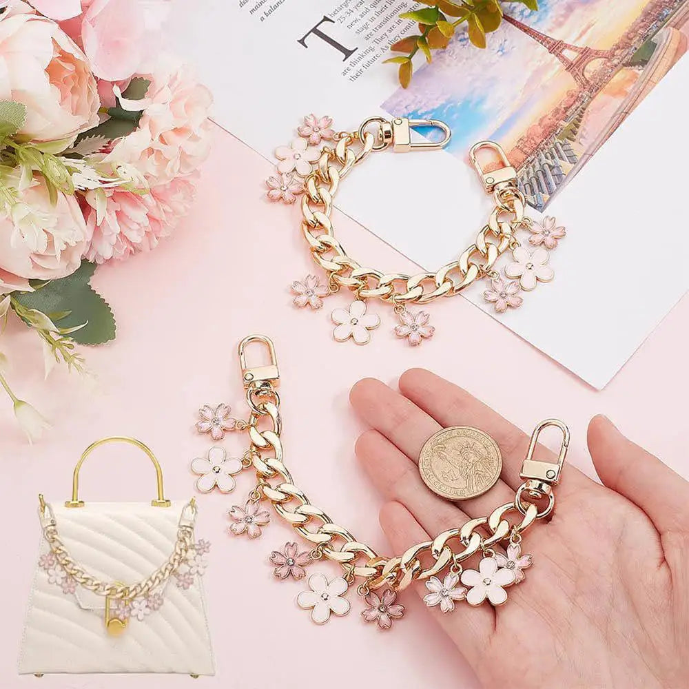 Accesorio de corazón dorado y cadena de flores de cerezo junto a un ramo floral rosa y un bolso blanco acolchado.