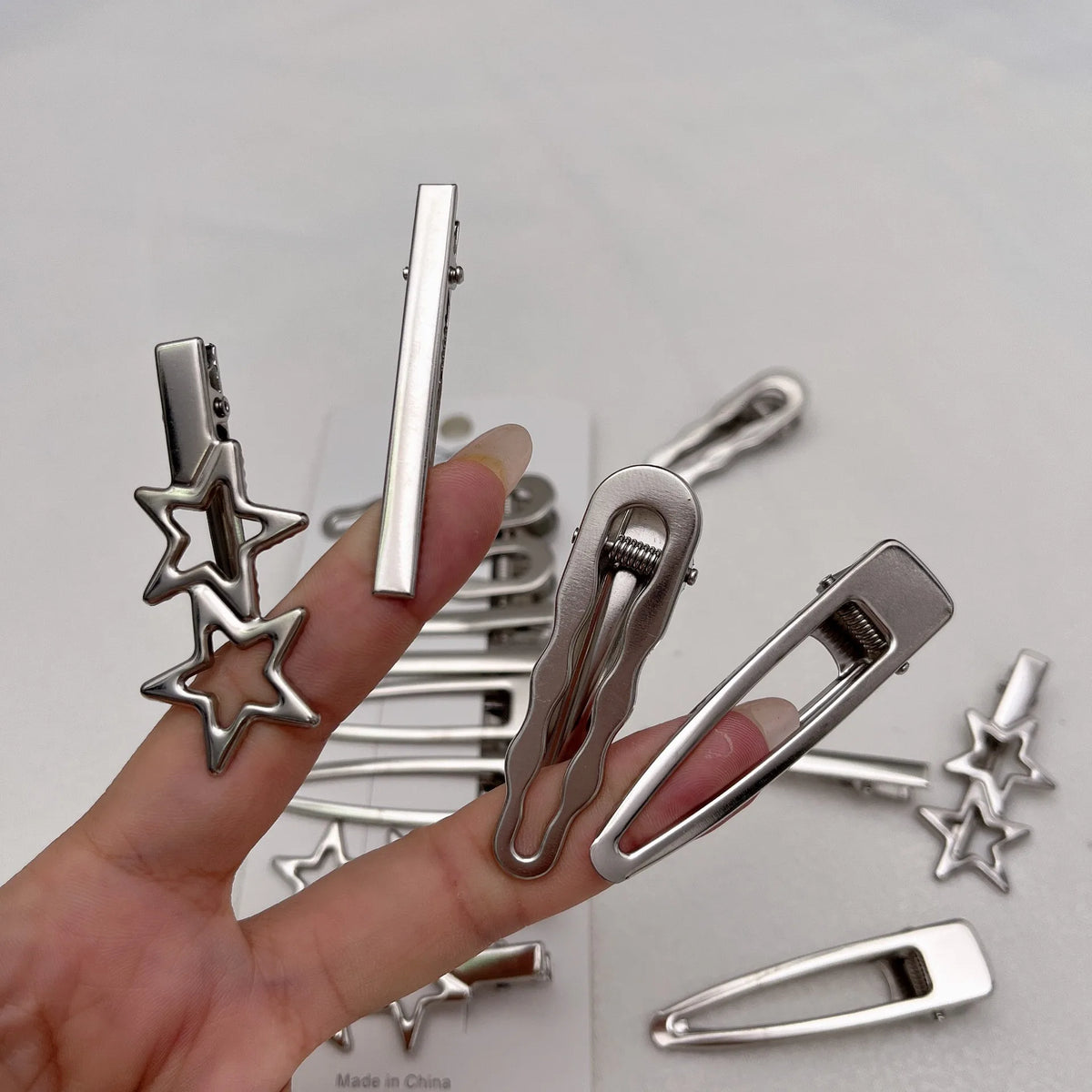 A hand holds a set of silver metal star hairpins and various clips, showing the collection of pins.