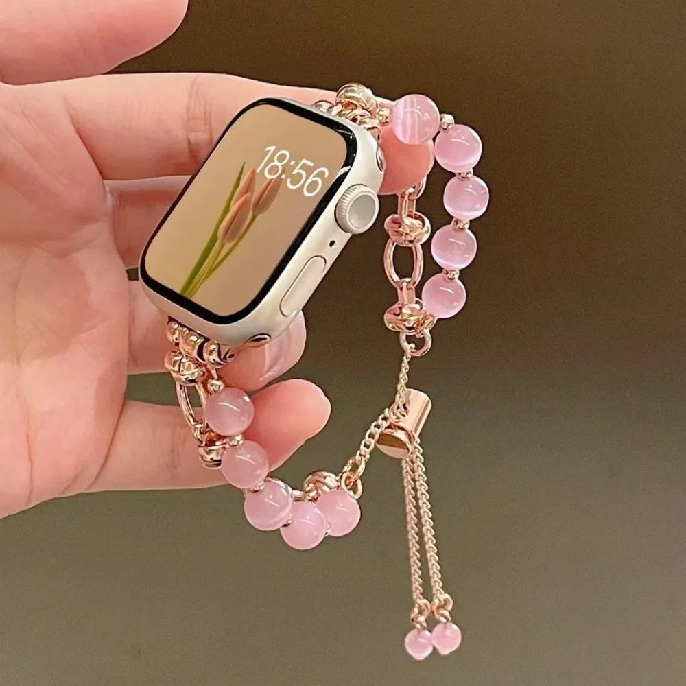 Eine Hand hält ein verstellbares Metallarmband mit rosa Kristallperlen und ein Smartphone, das 18:56 anzeigt.