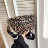 A leopard print PU leather crossbody bag with a black adjustable strap is shown hanging on a white door frame.