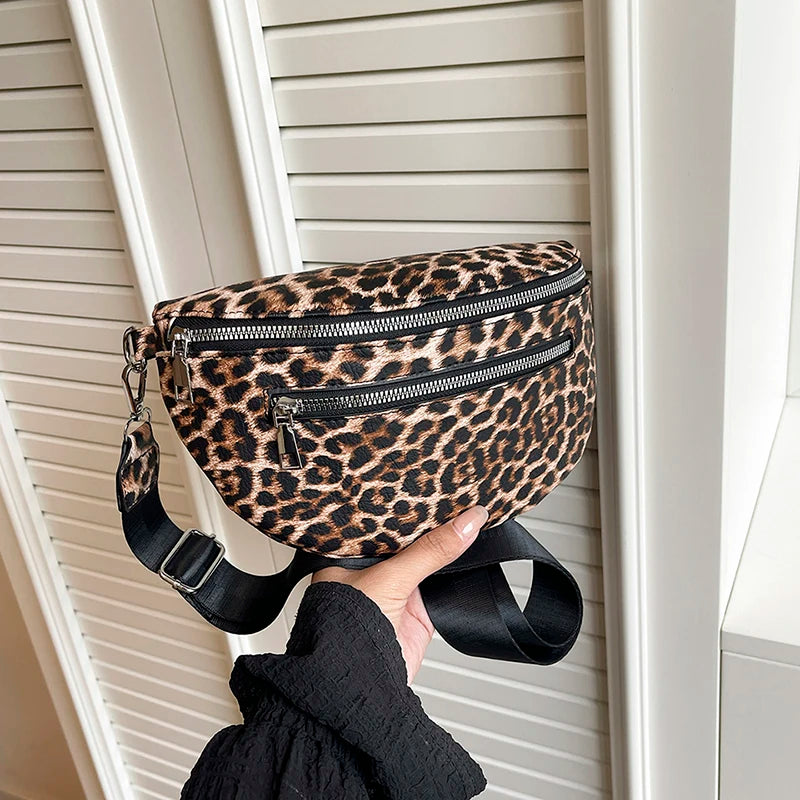 A leopard print PU leather crossbody bag with a black adjustable strap is shown hanging on a white door frame.