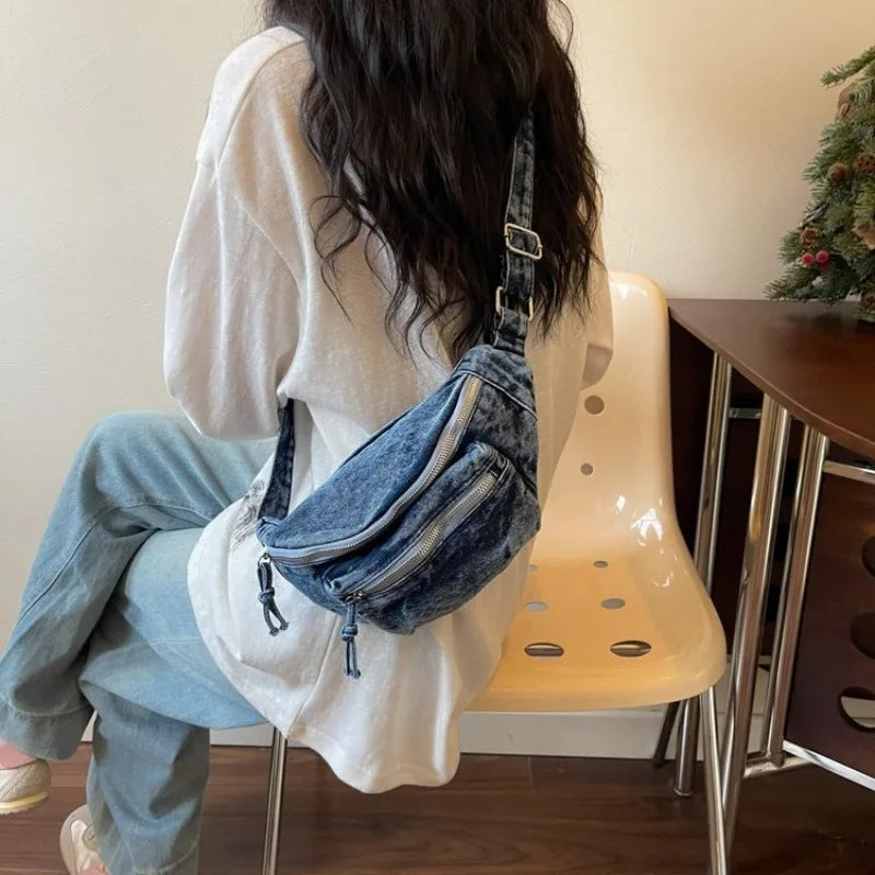 Une personne portant un pull clair et un jean tient un sac bandoulière en denim vintage délavé.