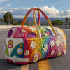 A colorful quilted travel duffle bag shaped like a vintage van is resting on asphalt.