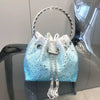 A light blue crystal-embellished evening clutch with a silver chain handle displayed on a glass surface.