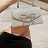 Un bolso de mano con lazo brillante plateado sostenido por una mano contra un fondo claro.