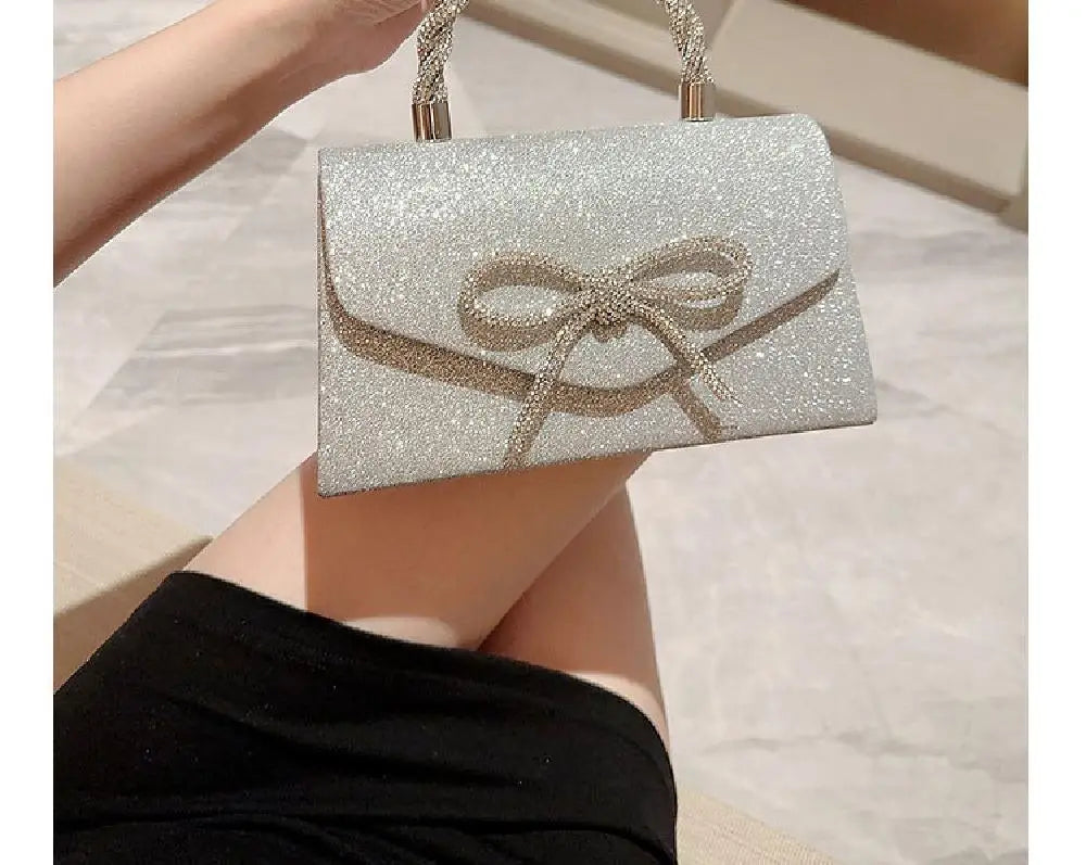 Un bolso de mano con lazo brillante plateado sostenido por una mano contra un fondo claro.