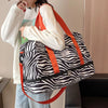 A person is carrying an orange and white patterned nylon travel duffle bag over their shoulder.
