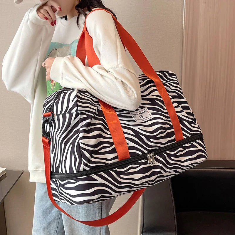 A person is carrying an orange and white patterned nylon travel duffle bag over their shoulder.