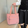 A pink canvas tote bag with light pink straps is held by a person against a light background.