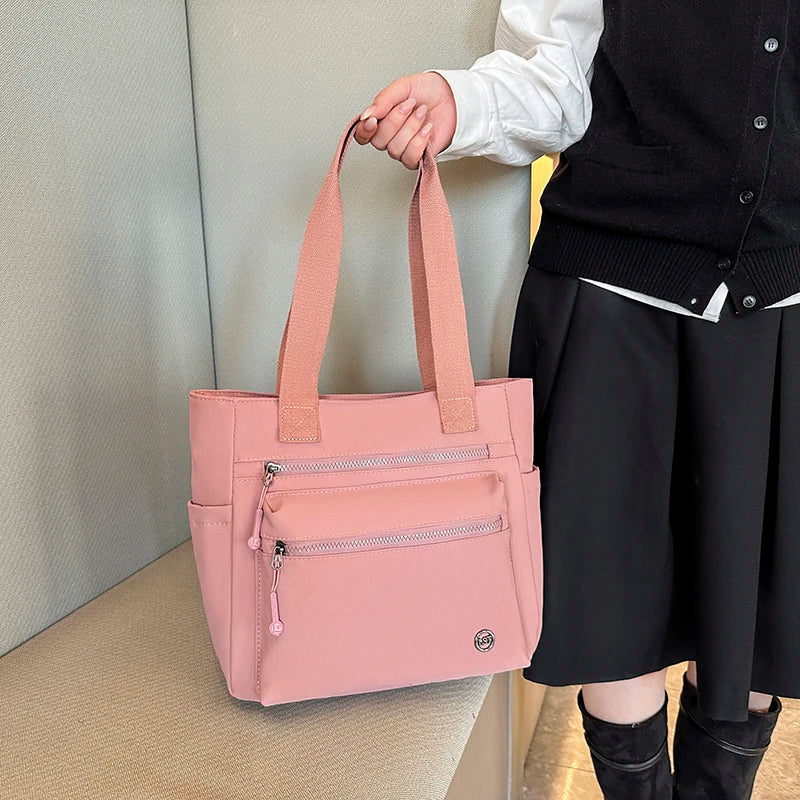 A pink canvas tote bag with light pink straps is held by a person against a light background.