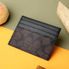A black PU leather card holder with a textured rose gold pattern rests on a bright yellow surface.
