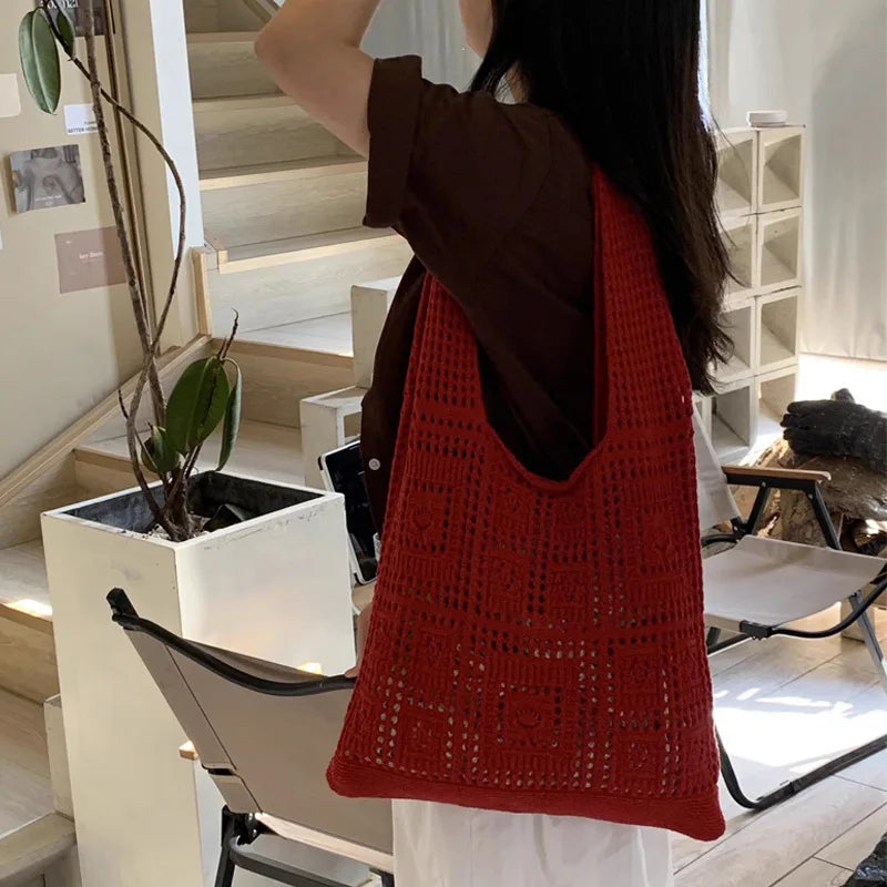 A woman is holding a red knitted shoulder bag with a mesh pattern in a vertical shot.