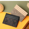 A stack of three elegant PU leather card holders in black, beige, and brown tones resting on an orange surface.