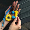 A hand holds a D-Shape nylon fitness keychain featuring yellow and blue components.
