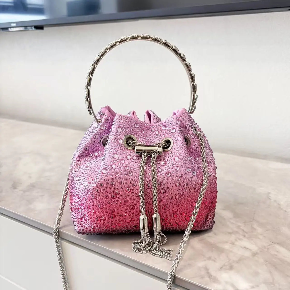 A pink crystal-embellished evening clutch with a silver chain strap resting on a light surface.