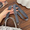 A hand holds a gray adjustable wide shoulder strap for bags or cameras next to a silver chain strap and a silver bag.