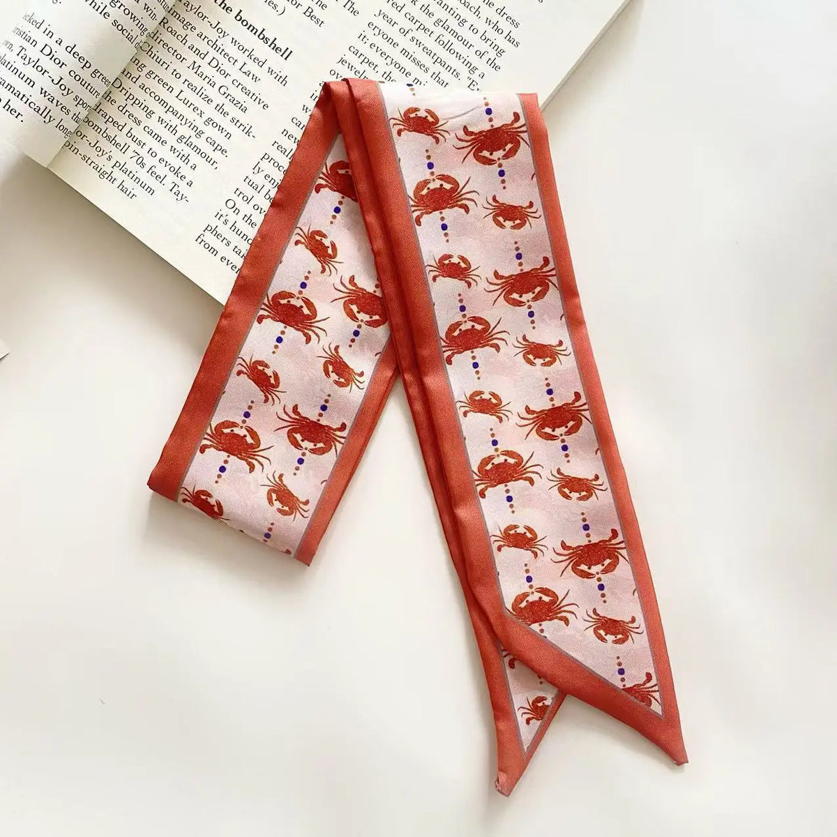 Foulard pour cheveux en soie rose avec un motif d'insectes rouges et oranges sur fond beige.