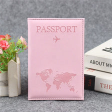 Pink PU leather passport cover with a silver airplane design resting on a gray surface.