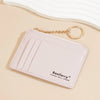 A light pink leather card holder wallet with ribbed texture and a gold chain keychain resting on a beige surface.