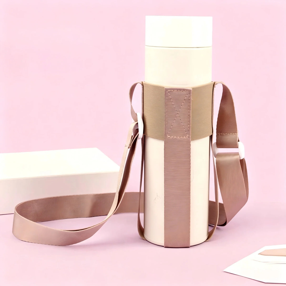 A beige crossbody sling water bottle bag with a light pink background and white box.