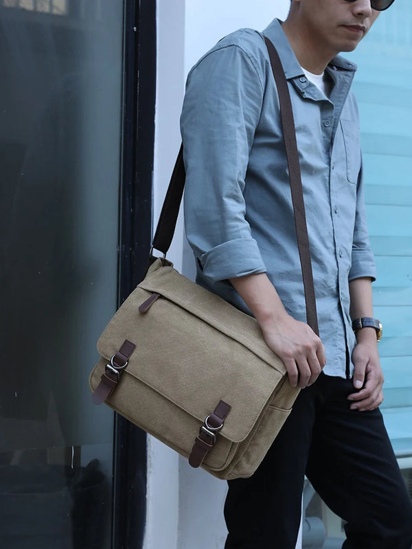 A person is holding a tan canvas laptop messenger bag with brown leather straps against a light background.