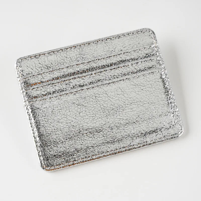 A silver metallic leather card holder with embossed lines and a textured surface.