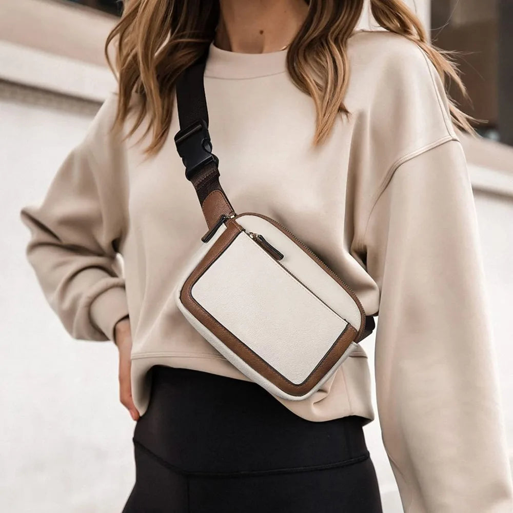 A woman wearing a beige sweatshirt and black leggings, carrying a tan and white PU leather crossbody bag.