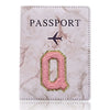 Cubierta de pasaporte de cuero marmolado rosa con una Q dorada y un icono de avión.