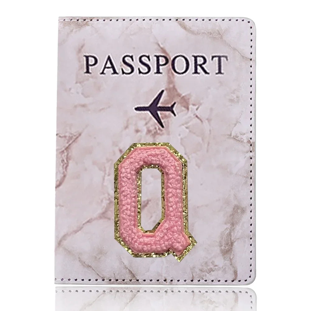 Cubierta de pasaporte de cuero marmolado rosa con una Q dorada y un icono de avión.