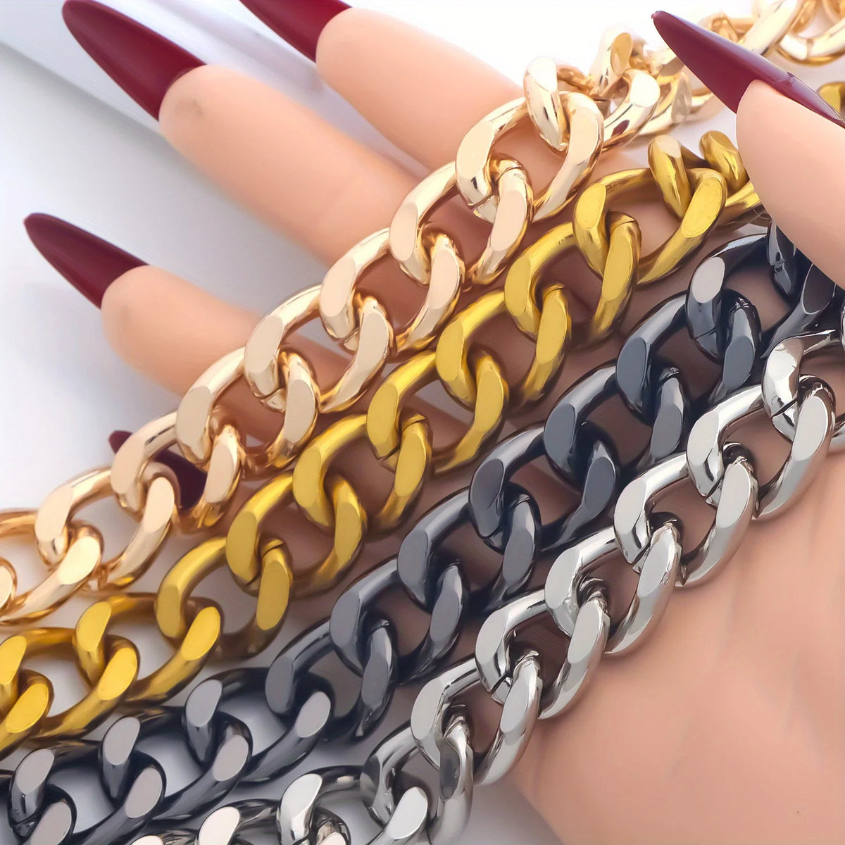 A hand holds several thick metal purse chain replacement straps in gold, yellow, and silver finishes.