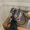 A close-up of a floral drawstring bucket bag in black and white patterned fabric with a gold hardware, resting on a wooden su