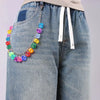 A silver chain necklace featuring colorful dice dangling from the chain, worn on a denim jean pocket.