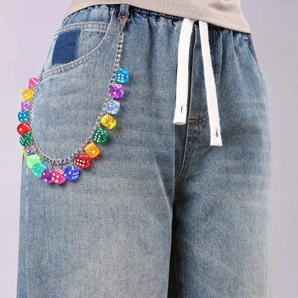 A silver chain necklace featuring colorful dice dangling from the chain, worn on a denim jean pocket.