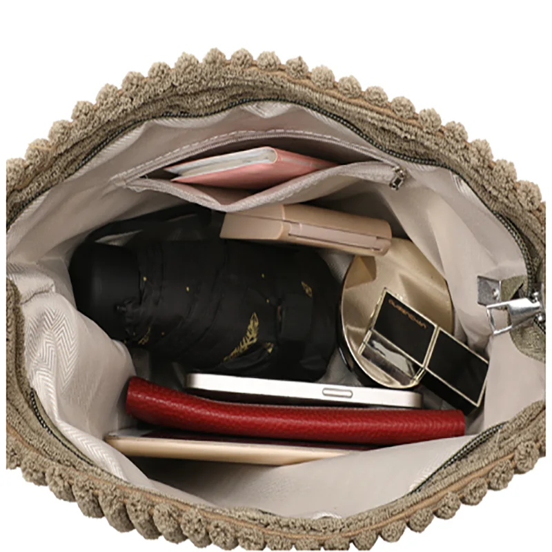 Un sac en velours côtelé beige ouvert, montrant divers accessoires comme un appareil photo, des lunettes de soleil et un smar
