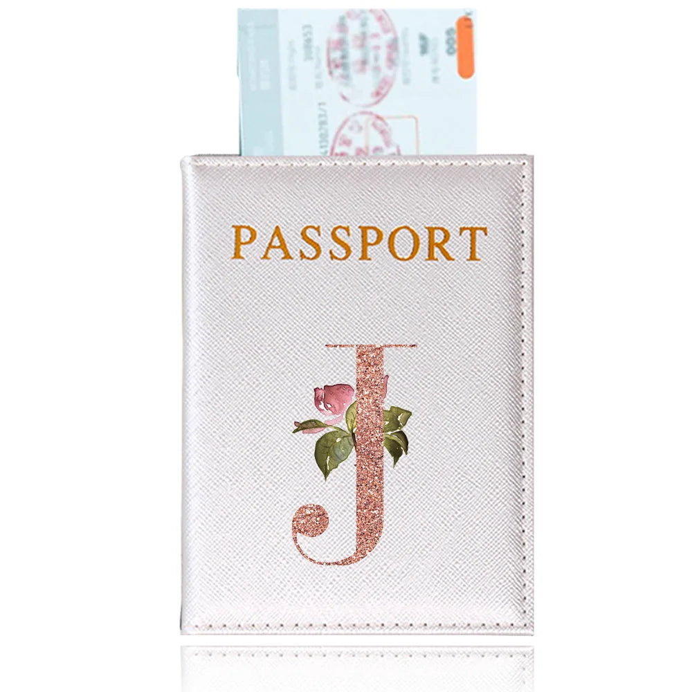 A pink leather passport holder with a gold embossed letter J and a passport visible behind it.