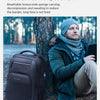 Ein Mann mit blauer Strickmütze und grüner Jacke sitzt neben einem schwarzen wasserdichten Rucksack im Freien.